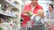 Young woman with a toddler in a cart shopping in a supermarket. Department of vegetables and herbs, salad in the package