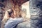 Young woman tourist looking into the distance through ancient stone window in old fortress during sunset in old European city. Con