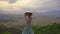 A young woman tourist stands on a mountain top with an amazing view on a valley. She wears an Asian hat