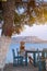 Young woman tourist in straw hat sitting at cliff cafe with sea view at Ermioni, Greece