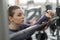 A young woman trains in the gym. Tired face, hands resting on the barbell.