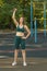 Young woman trains with a kettlebell on a street sports ground on a sunny day.