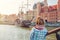 Young woman traveler with checked shirt and scarf looking at medieval wooden ship and embankment of Motlawa river