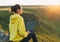 Young woman traveler freelancer in yellow hoodie with opened laptop on the beautiful view background