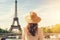 Young woman traveler in hat looking at Eiffel tower in Paris, France, Rear view of woman tourist in sun hat standing in front of