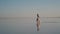 Young woman traveler with a little girl in a shirt running along the salt lake, which reflects the sky against the