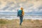 Young woman traveler in a yellow jacket walks along the coast of the north sea with a backpack, wild tourism and adventures in