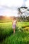 Young woman travelling in Asia, walking with rattan backpack in rice paddies during rainy season in Bali, freedom