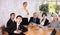 Young woman turning on presentation on projector while office coworkers of different ages making notes at table with