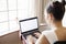 A young woman types on her laptop. She is relaxed.