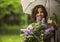 Young woman under an umbrella with a bouquet of lilac in hand during rain.