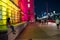 A young woman uses a smartphone while sat on a wall next to colorfully lit County Hall at night