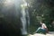 Young woman using her mobile next to McLean falls located in the South Island of New Zealand