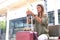 Young woman using her smartphone and resting upon her suitcase, waiting for the train at a railway station