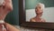 Young woman using jade facial roller for face massage sitting by the bathroom mirror