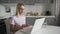 Young woman using laptop computer and phone at kitchen. Business woman working on notebook