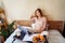 Young woman using laptop in a cozy home atmosphere on the bed with a cup of coffee and delicious fruits with pastries. Freelancer