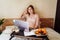 Young woman using laptop in a cozy home atmosphere on the bed with a cup of coffee and delicious fruits with pastries. Freelancer