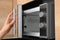 Young woman using microwave oven in kitchen