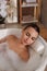 Young woman using pillow while enjoying bubble bath indoors