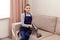 A young woman vacuums the sofa with a cleaning vacuum cleaner.