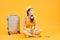 Young woman waiting for flight, sitting on floor near her suitcase, wearing face mask to prevent coronavirus