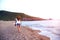 Young woman walk on an empty wild beach towards celestial beams of light falling from the sky