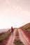 Young woman walkin on dirt path country road on the hill at even