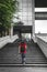 young woman walking alone climb the stairs in a modern neighborhood of a big city while holding an umbrella under rain