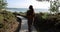 Young woman walking alone at seaside on wooden path next to ocean on clear sunny day