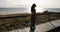 Young woman walking alone at seaside on wooden path next to ocean on clear sunny day