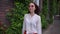 Young woman is walking along brick building with ivy