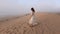 Young woman walking along sea shore sand beach in fog rainy day. Girl in long dress enjoy view on sand dune near ocean