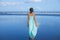 Young woman walking barefoot on empty beach. Full body portrait. Slim Caucasian woman wearing long dress. View from back. Summer