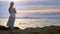 Young woman walking on a rocky and enjoying the view of the sunset, splashing waves