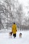 Young woman is walking in a snowy winter park with her two dogs. Back view