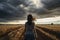 Young woman walking on wheat field and looking at stormy sky