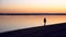 A young woman walks along the beach along the river at sunrise. Silhouette of a girl. Goes to meet the dawn.