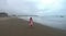 A young woman walks along the empty coast, leaving traces on the sand in the fog