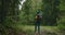 A young woman walks along a road in the woods with a backpack in slow motion. A female traveler in a yellow sweater and