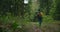 A young woman walks along a road in the woods with a backpack in slow motion. A female traveler in a yellow sweater and