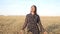 Young woman walks in a dress on a field of ripe wheat and smiles