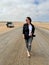 Young woman walks on highway in desert. Girl on center of the road, barefoot.