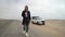 Young woman walks on highway, her car at roadside parked in desert. White SUV.