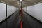 A young woman walks on a red line down a subway corridor while looking at her cell phone wearing a face mask