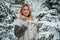 A young woman walks through a winter coniferous forest in search of a beautiful christmas tree for her home.