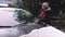 Young woman in warm clothes, using ice scraper, scraping ice from the windshield