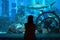 Young woman watch fishes and sharks in beautiful blue aquarium in Dubai