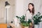 Young woman watering flowerpots at home. Casual lifestyle series in modern scandinavian interior