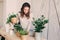 Young woman watering flowerpots at home. Casual lifestyle series in modern scandinavian interior